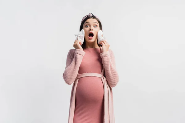 Schockierte und schwangere Frau mit winzigen Stiefeln auf weißem Grund — Stockfoto