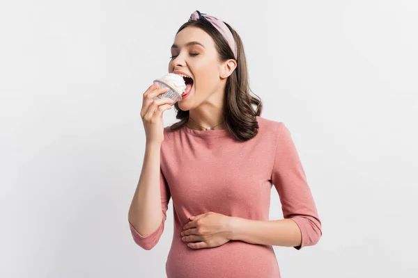 Mulher grávida alegre com olhos fechados comendo cupcake isolado em branco — Fotografia de Stock