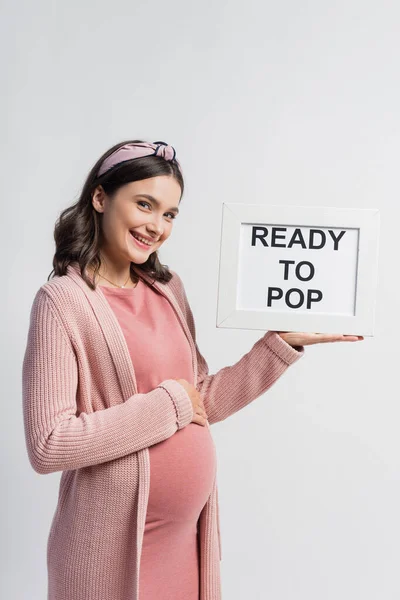 Joyeuse femme enceinte tenant conseil avec prêt à pop lettrage isolé sur blanc — Photo de stock