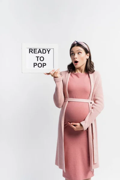 Shocked pregnant woman looking at board with ready to pop lettering isolated on white — Stock Photo