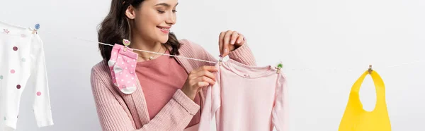 Panoramic crop of woman hanging baby clothes on clothing line isolated on white — Stock Photo