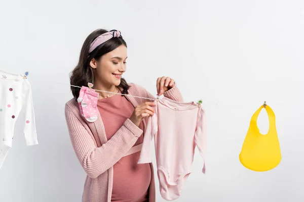 Pregnant woman hanging baby clothes on clothing line isolated on white — Stock Photo