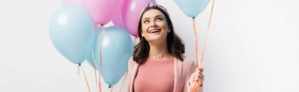 Panoramic crop of joyful woman in headband holding balloons and looking up isolated on white — Stock Photo