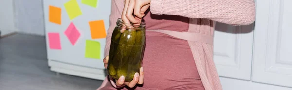 Заголовок сайту вагітної жінки, що тримає консервовану банку з огірками вдома — стокове фото