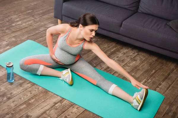 Vue grand angle de la femme enceinte en tenue de sport étirant sur tapis de fitness — Photo de stock