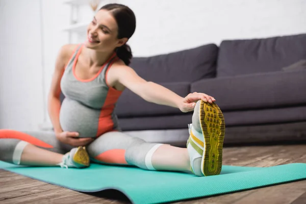 Selective focus of pleased pregnant woman in sportswear stretching on fitness mat — Stock Photo