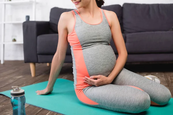 Vue recadrée de la femme enceinte heureuse en vêtements de sport assis sur tapis de fitness — Photo de stock