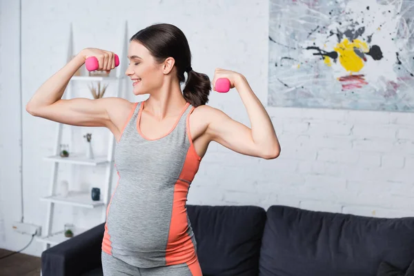 Joyeuse femme enceinte exerçant avec des haltères roses à la maison — Photo de stock