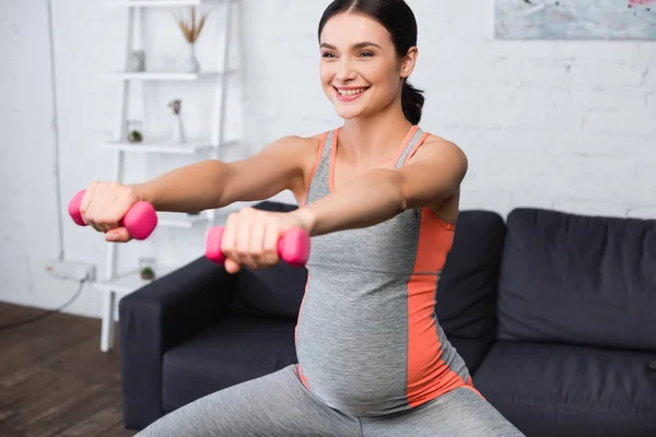 Selektiver Fokus der zufriedenen Schwangeren, die zu Hause mit rosa Kurzhanteln trainiert — Stockfoto