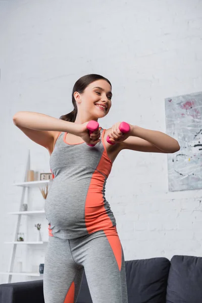 Femme enceinte et joyeuse travaillant avec des haltères à la maison — Photo de stock