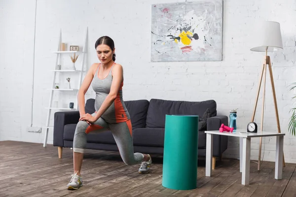 Brunette and pregnant woman exercising near sport equipment in living room — Stock Photo