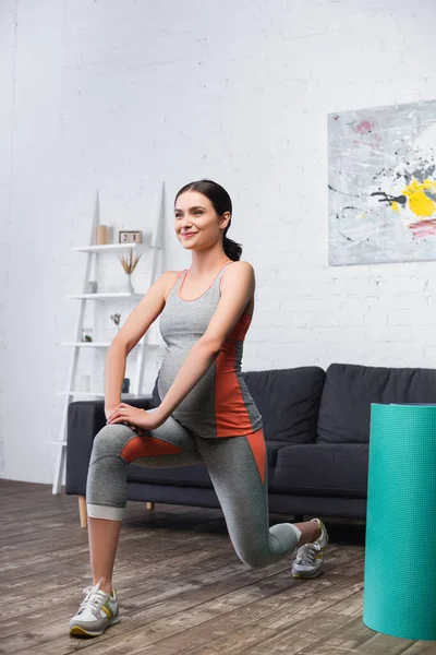 Donna gioiosa e incinta che esercita vicino al tappeto fitness in soggiorno — Foto stock