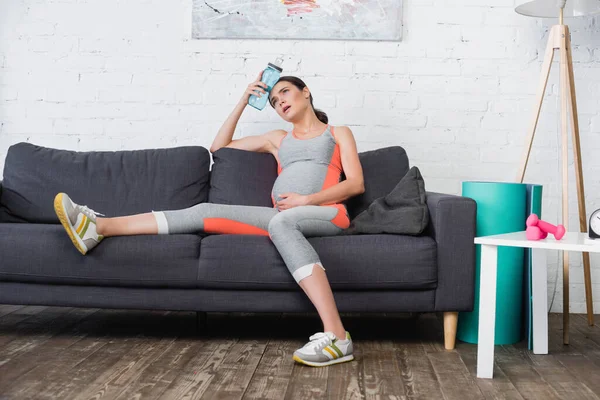 Müde und schwangere Frau liegt auf Sofa und hält Sportflasche mit Wasser — Stockfoto