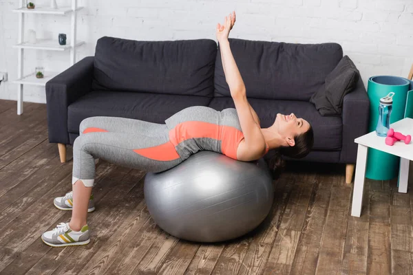 Mujer embarazada alegre haciendo ejercicio en la pelota de fitness en la sala de estar - foto de stock