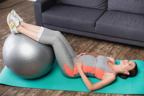 Брюнетка беременная женщина работает с фитнес-мяч возле дивана — стоковое фото