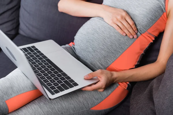 Teilbild einer Schwangeren in Sportbekleidung mit Laptop zu Hause — Stockfoto