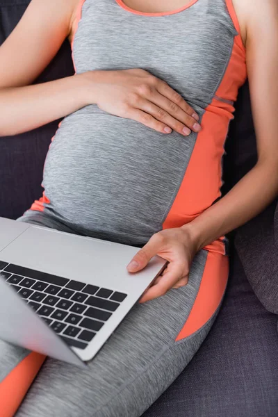 Cropped view of pregnant woman in sportswear using laptop at home — Stock Photo