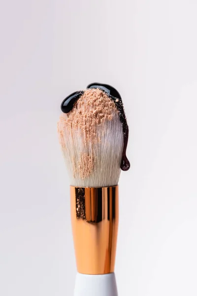 Vista de cerca del cepillo cosmético con polvo facial y goteo de líquido negro aislado en blanco - foto de stock
