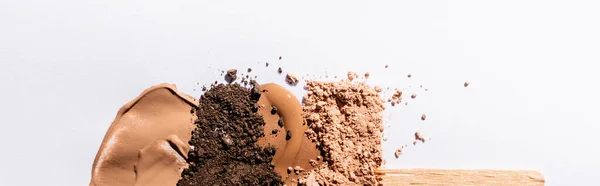 Top view of beige face foundation brushstrokes and eyeshadow powder with wooden stick on white background, panoramic shot — Stock Photo