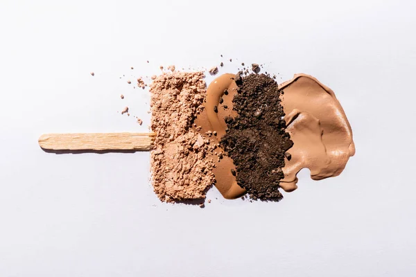 Top view of beige face foundation brushstrokes and eyeshadow powder with wooden stick on white background — Stock Photo