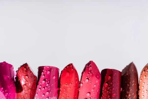 Vue rapprochée des rouges à lèvres humides en rangée isolés sur blanc — Photo de stock