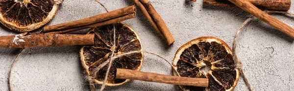 Tiro panorâmico de pedaços de laranja seca e paus de canela no fundo cinza — Fotografia de Stock