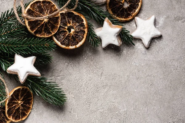 Vue du dessus de la branche de pin avec des morceaux d'orange séchée et des biscuits sur fond gris — Photo de stock