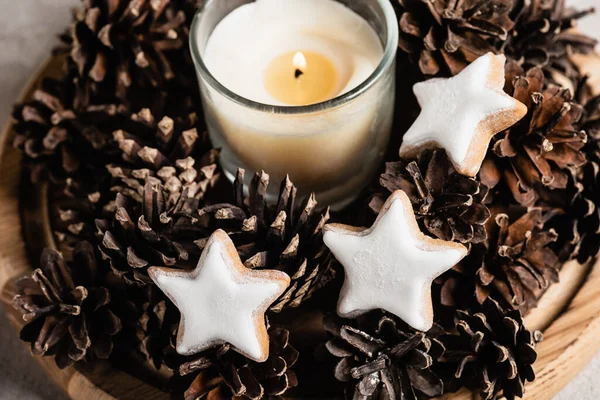 Scented candle with pine cones and cookies on wooden plate — Stock Photo