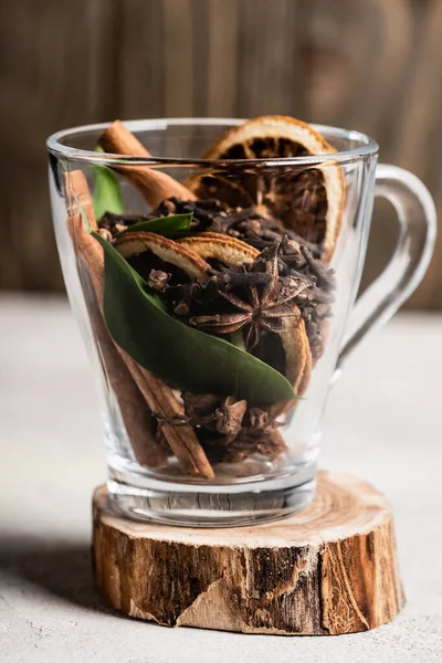 Selective focus of glass cup with spices and orange dried slices on wooden stand — Stock Photo