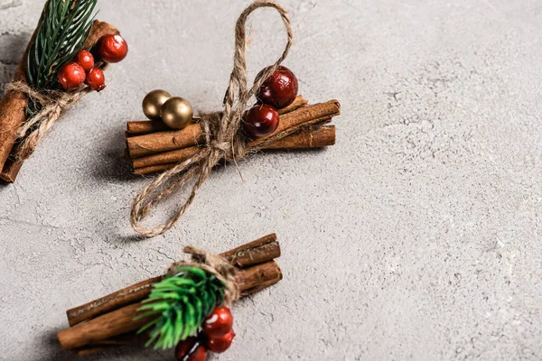 Cinnamon sticks with red beads on textured and grey background — Stock Photo
