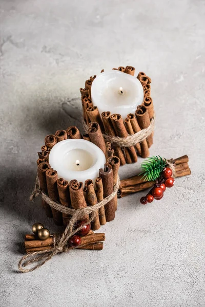 Ароматизированные свечи, украшенные коричными палочками на текстурированном и сером фоне — стоковое фото