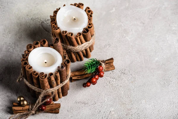 Bougies parfumées décorées avec des bâtons de cannelle sur fond gris et texturé — Photo de stock