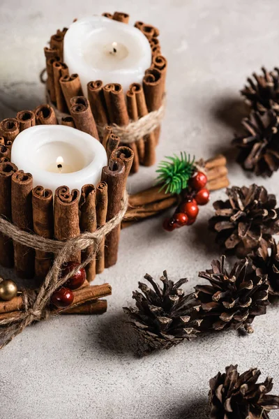 Scented candles decorated with cinnamon sticks near red beads and pine cones — Stock Photo