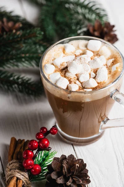 Selective focus of glass cup of cocoa near cinnamon sticks and pine cone — Stock Photo