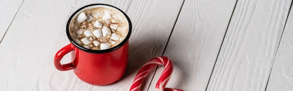 Imagen horizontal de taza roja de cacao cerca de bastón de caramelo sobre fondo de madera — Stock Photo