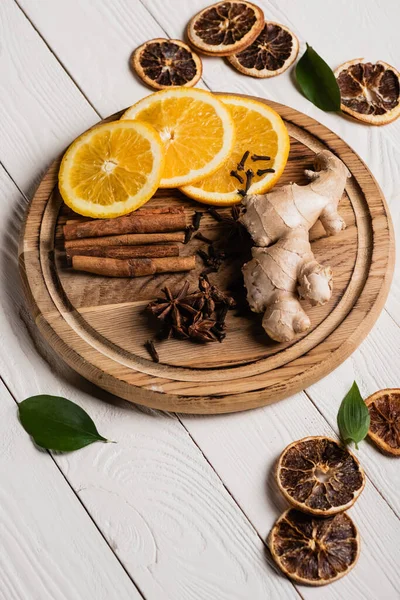 Fresh orange slices with spices and ginger root on wooden plate — Stock Photo