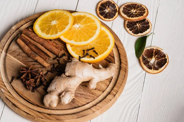 Placa de madera con especias, raíz de jengibre y rodajas de naranja sobre fondo de madera - foto de stock