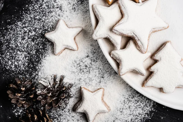 Top view of cookies on plate near pine cones covered with sugar powder — Stock Photo