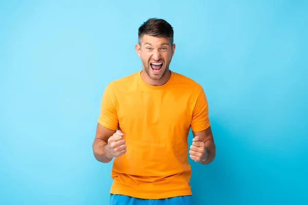 Animado homem com boca aberta e punhos apertados no azul — Fotografia de Stock