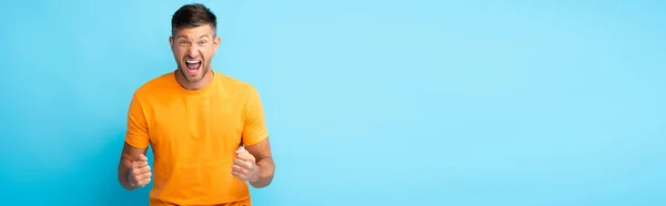 Hombre excitado con la boca abierta y puños apretados en azul, bandera - foto de stock