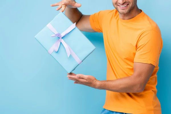 Обрізаний вид щасливого чоловіка в футболці, що тримає загорнуту подарункову коробку на синьому — стокове фото