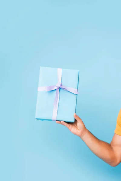 Обрезанный вид человека, держащего завернутую подарочную коробку на голубом — стоковое фото