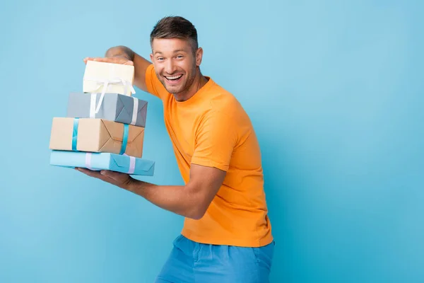 Homme heureux en t-shirt tenant des cadeaux enveloppés sur bleu — Photo de stock