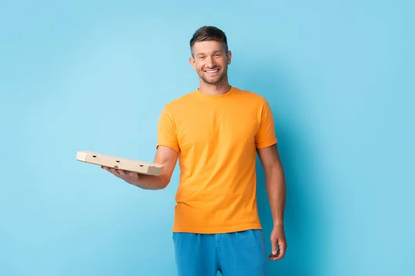 Pleased man in t-shirt holding carton pizza box on blue — Stock Photo