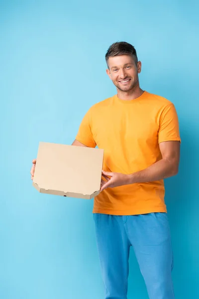 Gioioso uomo in t-shirt contenente scatola di cartone pizza su blu — Foto stock