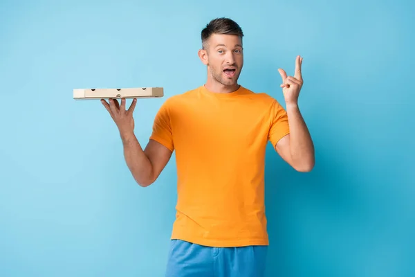Hombre con boca abierta sosteniendo caja de pizza de cartón y gestos en azul - foto de stock