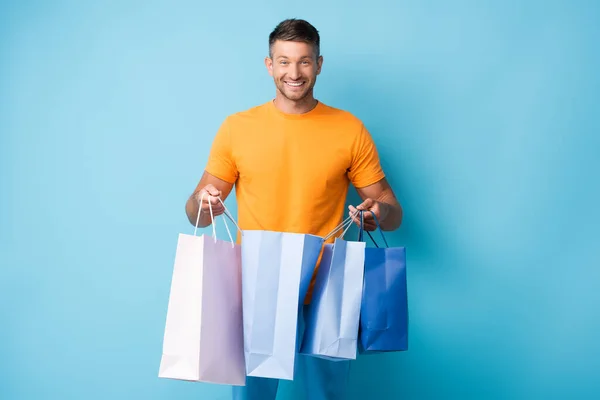 Hombre alegre en camiseta sosteniendo bolsas de compras en azul - foto de stock