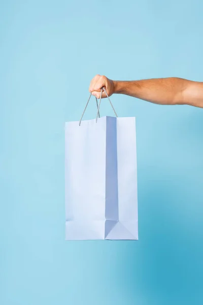 Cropped view of man in t-shirt holding shopping bag on blue — Stock Photo