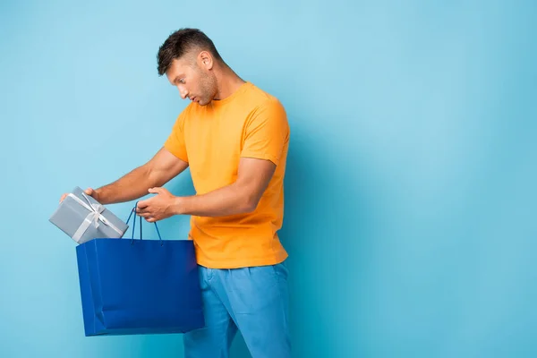 Mann im T-Shirt mit Einkaufstasche und Geschenkbox auf blau — Stockfoto