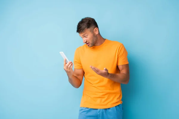 Uomo scontento in t-shirt con smartphone su blu — Foto stock